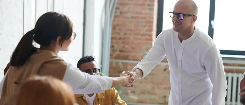 Un apretón de manos entre dos profesionales durante una reunión informal en una oficina con paredes de ladrillo expuesto.
